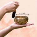 Load image into Gallery viewer, Full Moon Singing Bowl held in hand with wooden mallet, showing aged brass finish and size context.