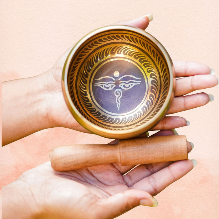 Wisdom Eye Singing Bowl with Wisdom Eye symbol inside, held in hand with wooden mallet and decorative inner border.