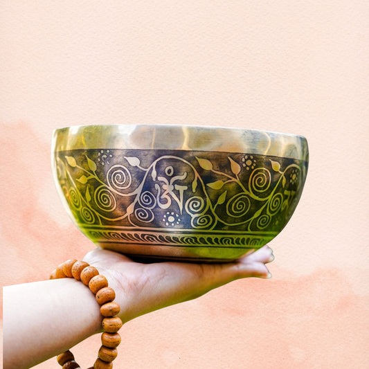 Tree of Life Singing Bowl held in hand, showing floral exterior engraving, aged brass finish.