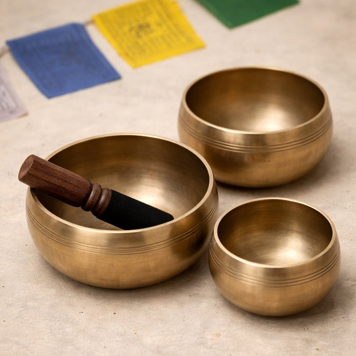 Three brass singing bowls on a textured surface with prayer flags in the background.