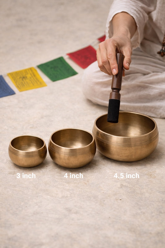 Three brass singing bowls with sizes labeled, being played on a mat with prayer flags.