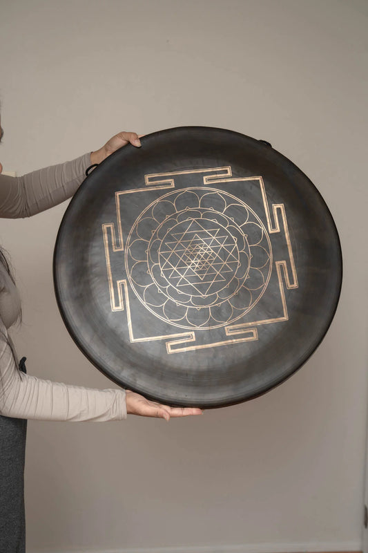 Divine Shri Yantra Gong with golden symbolic geometry mandala design on a dark aged metal surface, held by hand for sound practice and quiet listening use.