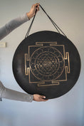 Load image into Gallery viewer, Divine Shri Yantra Gong with golden symbolic geometry mandala design on a dark aged metal surface, held by hand for sound practice and quiet listening use.
