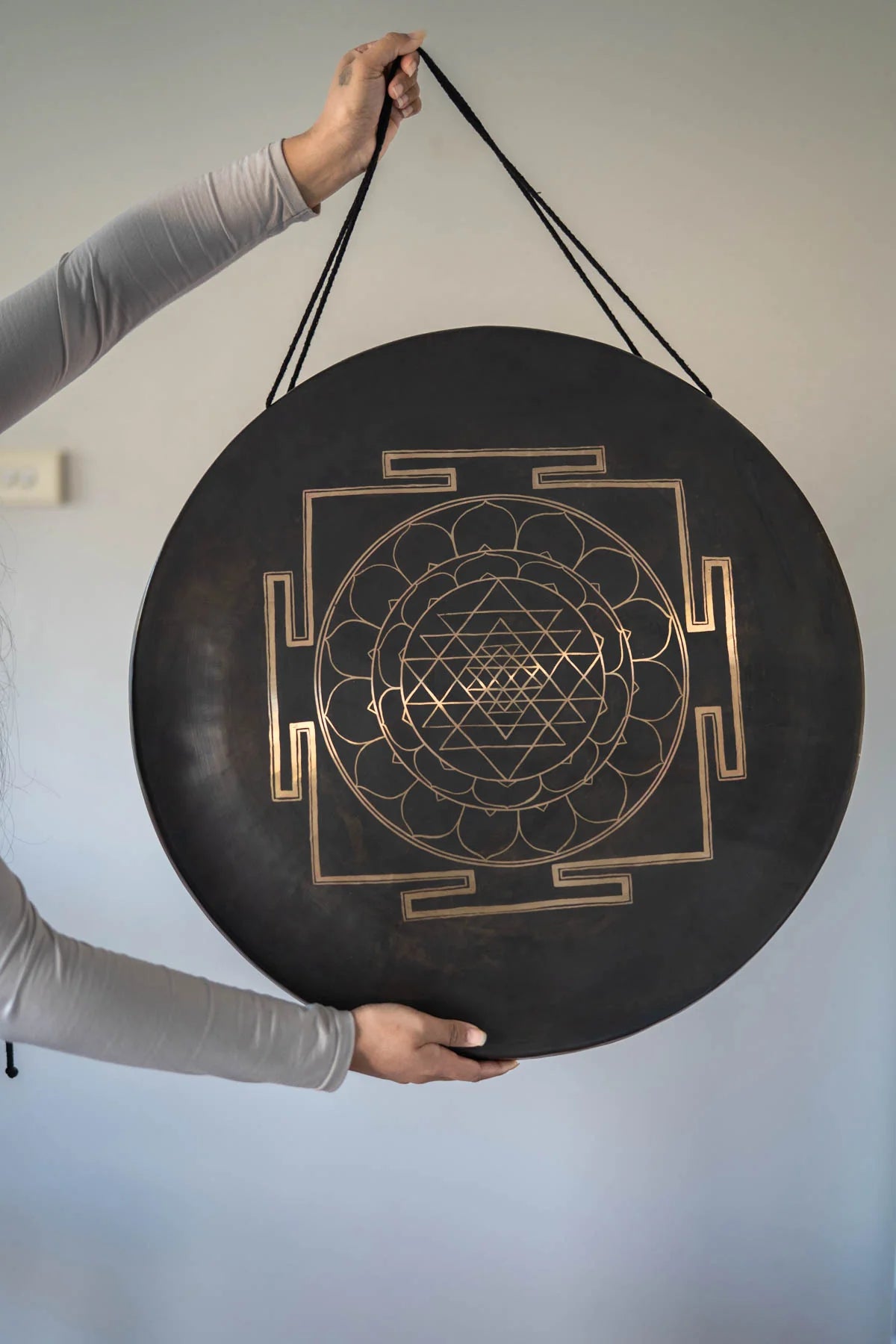 Divine Shri Yantra Gong with golden symbolic geometry mandala design on a dark aged metal surface, held by hand for sound practice and quiet listening use.