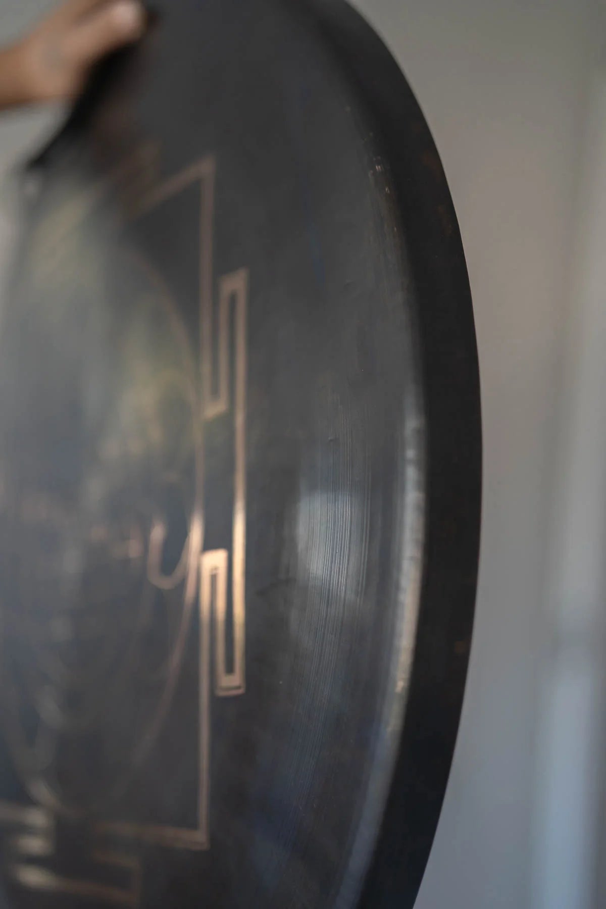Divine Shri Yantra Gong with golden symbolic geometry mandala design on a dark aged metal surface, held by hand for sound practice and quiet listening use.
