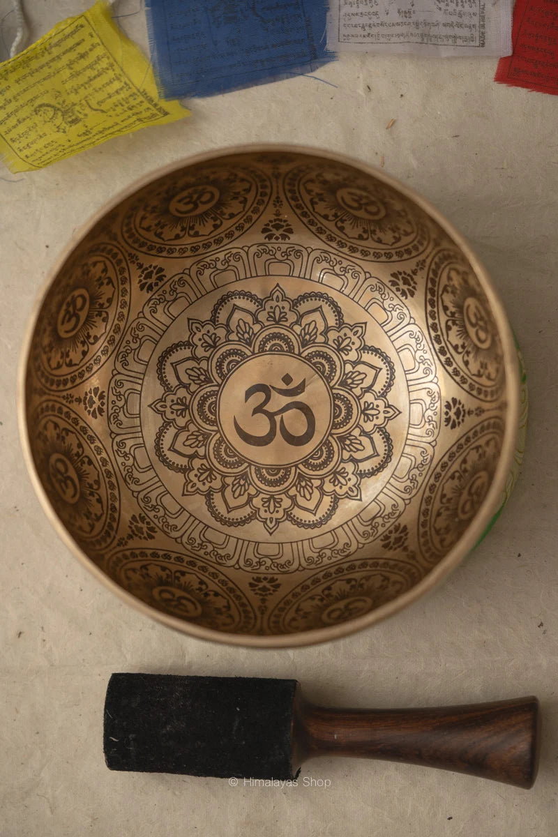 Om Mandala carved singing bowl with central Om symbol, detailed floral mandala engraving, repeated Om motifs, and wooden striker.