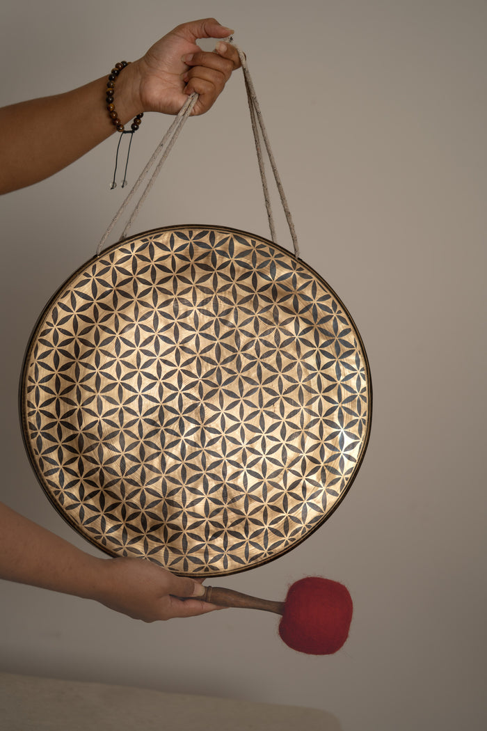 Flower of Life Gong with symbolic geometry engraving, held by hand with red mallet for harmony and balance.